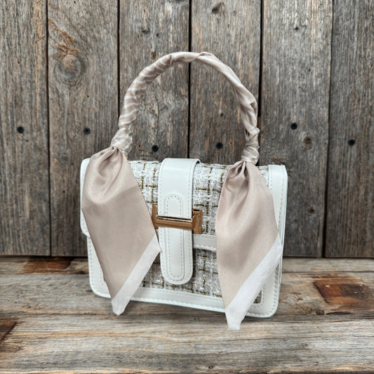 A white handbag with a gold clasp and beige fabric accents is displayed against a wooden background.