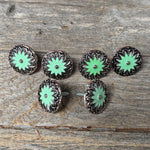 a collection of six green and black floral-patterned buttons arranged on a wooden surface.
