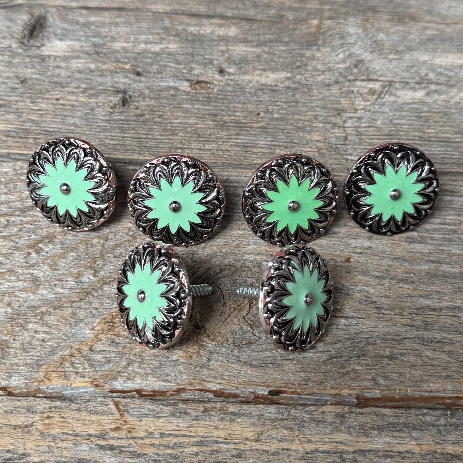a collection of six green and black floral-patterned buttons arranged on a wooden surface.