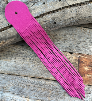 A pink leather fringe with a hole at one end, placed on a wooden surface.