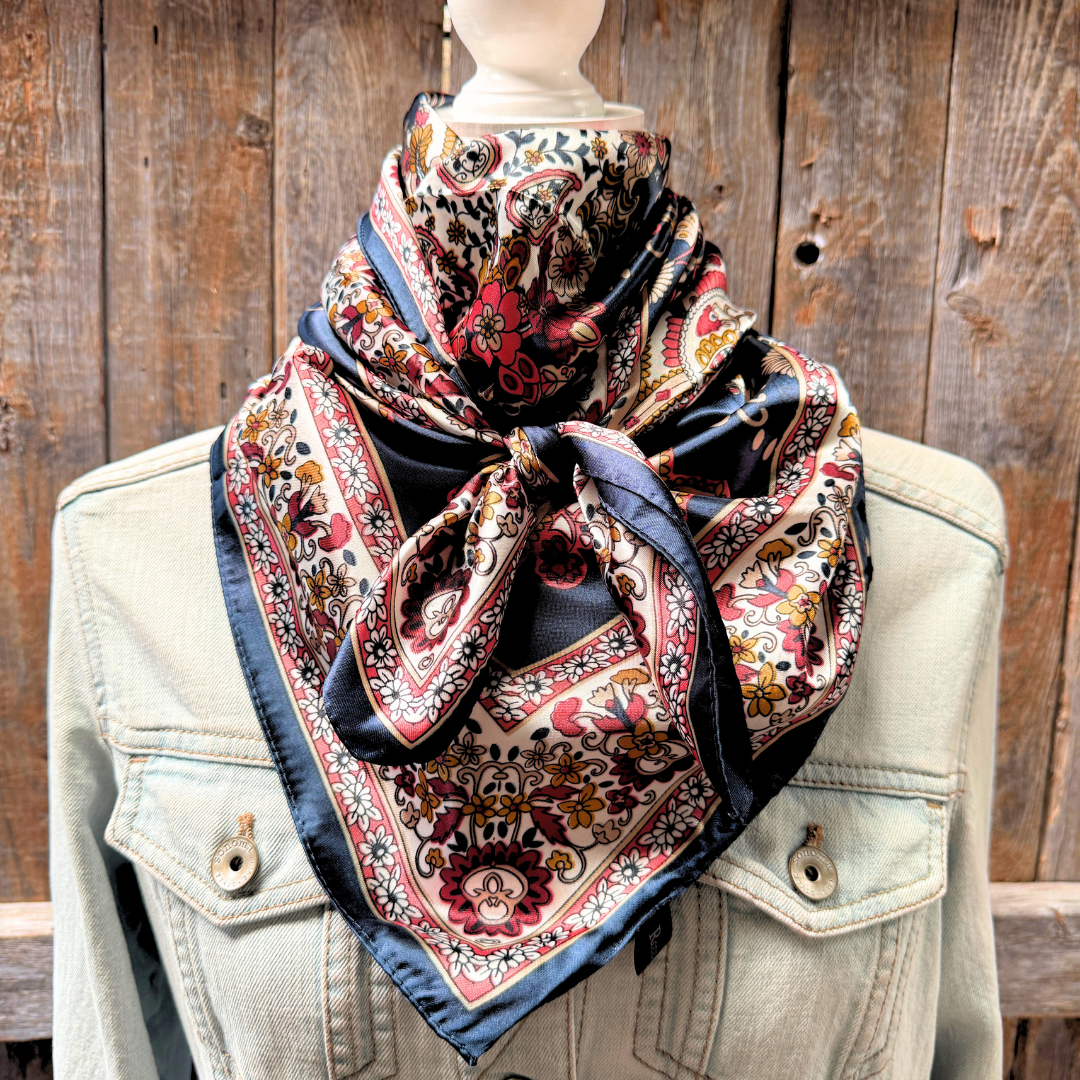 A navy, burgundy, and white floral and paisley patterned scarf displayed on a mannequin wearing a denim jacket.