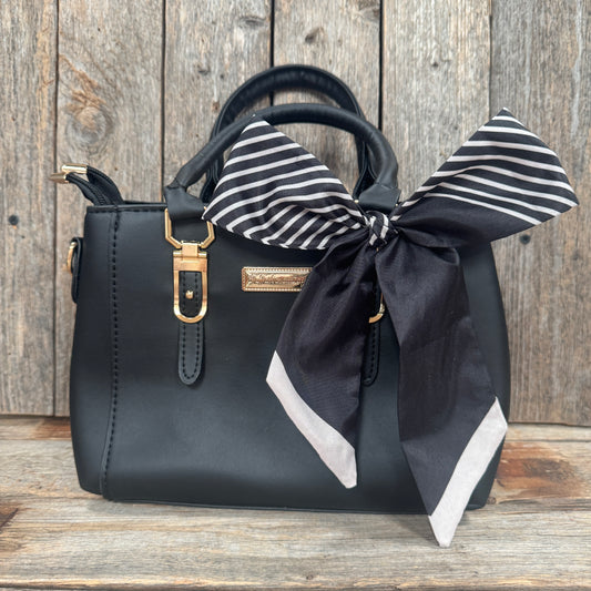 A black leather handbag with a gold-colored metal clasp and handle, and a black and white striped scarf tied around the handle.