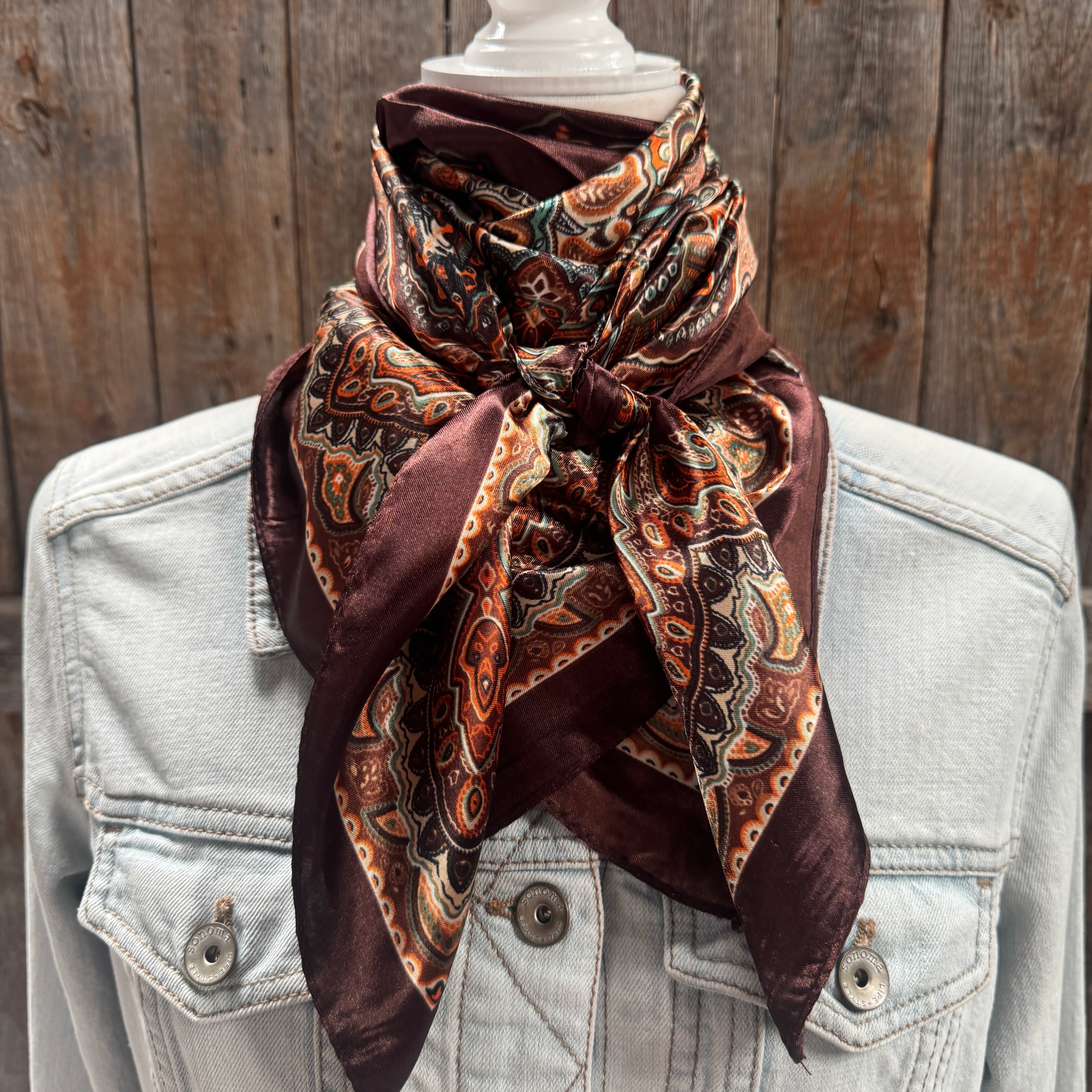 Patterned scarf draped over a light blue denim jacket against a wooden background