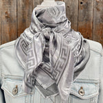 A silver floral jacquard pattern scarf displayed on a mannequin wearing a denim jacket.