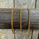 Three gold-toned bangle bracelets covered in small clear stones, displayed on a dark wooden dowel against a rustic wood plank background.