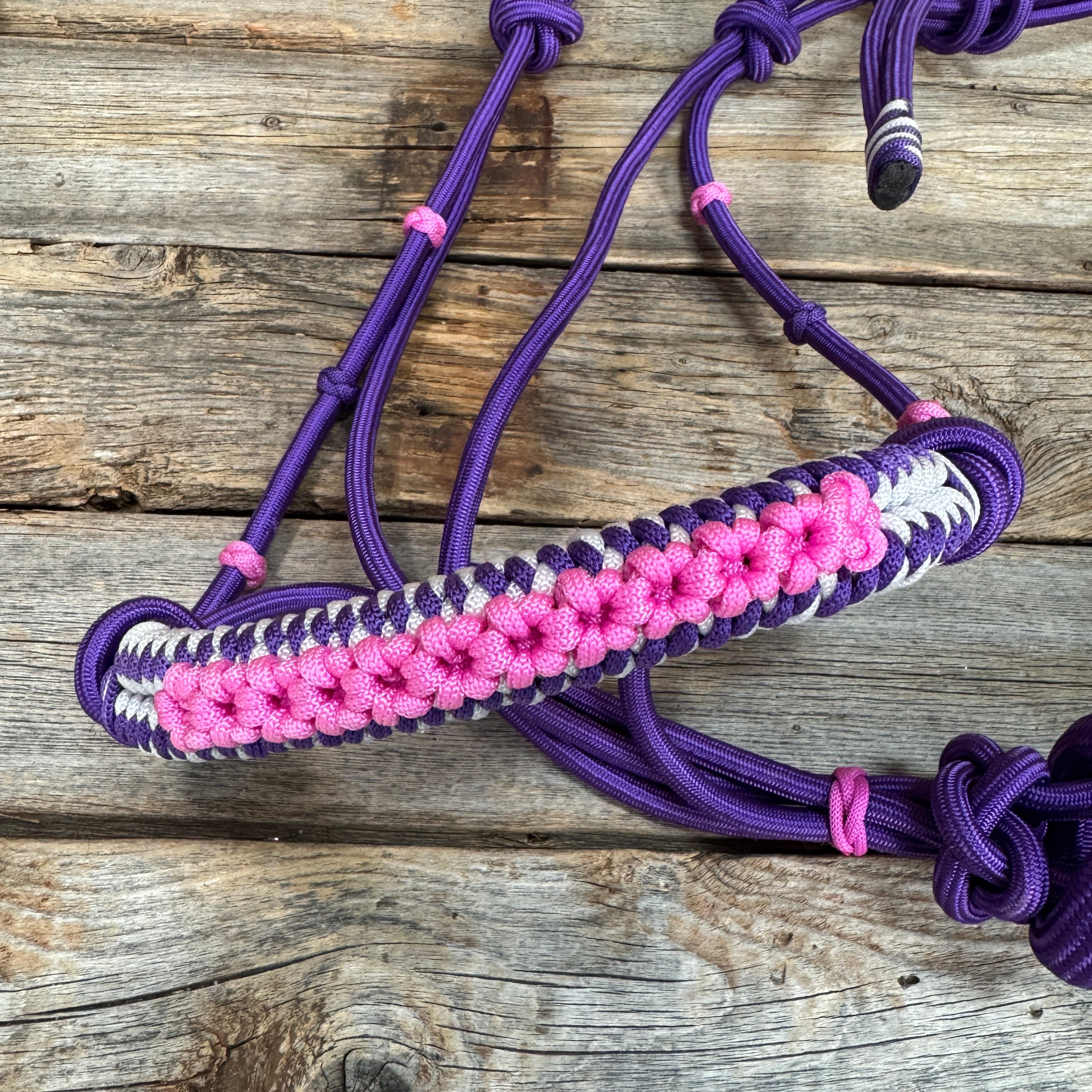 A purple paracord horse halter with a pink and white woven browband, displayed on a rustic wooden surface.