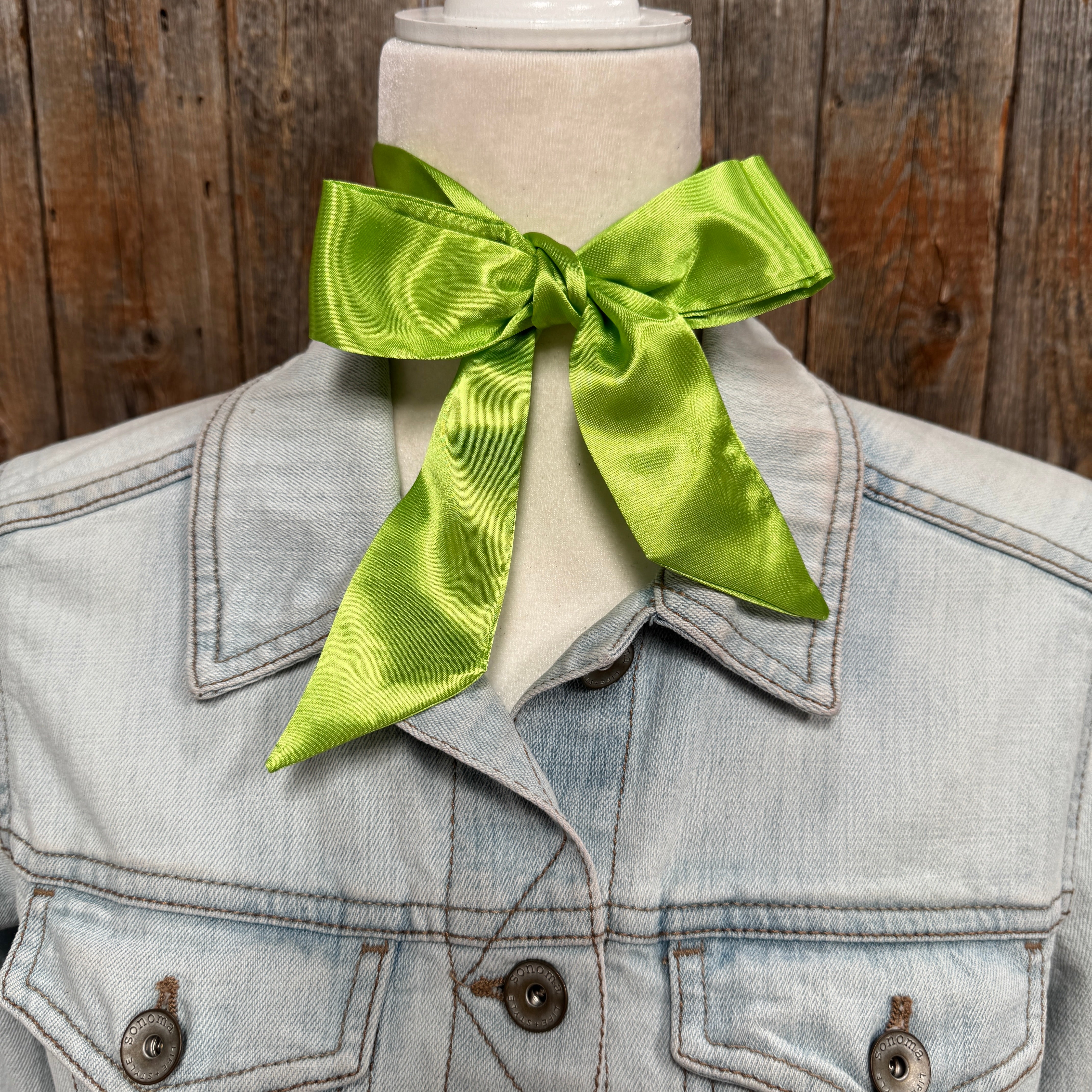 Light blue denim jacket with a large green bow on a wooden background