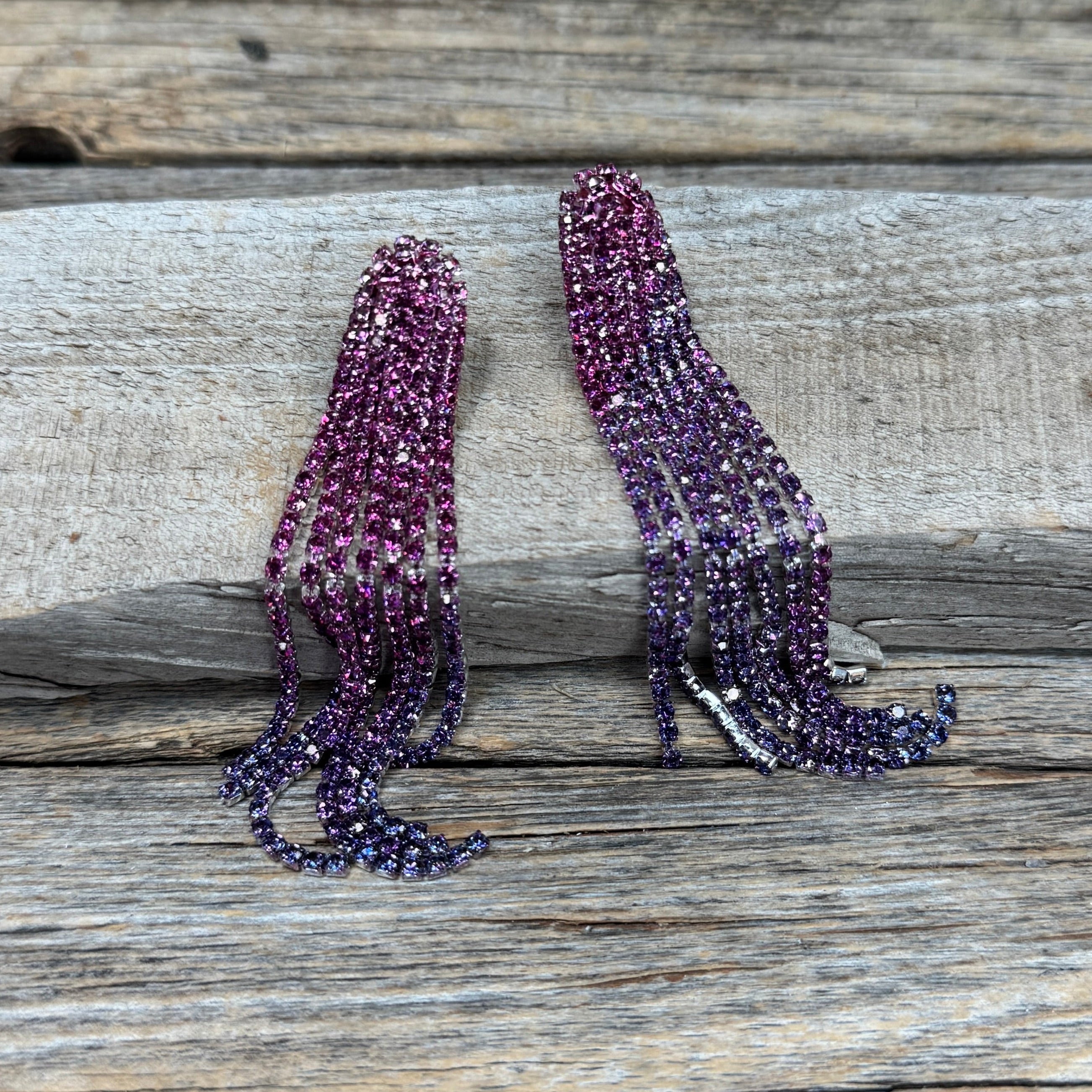 Long, dangling earrings with pink gemstones on a wooden surface