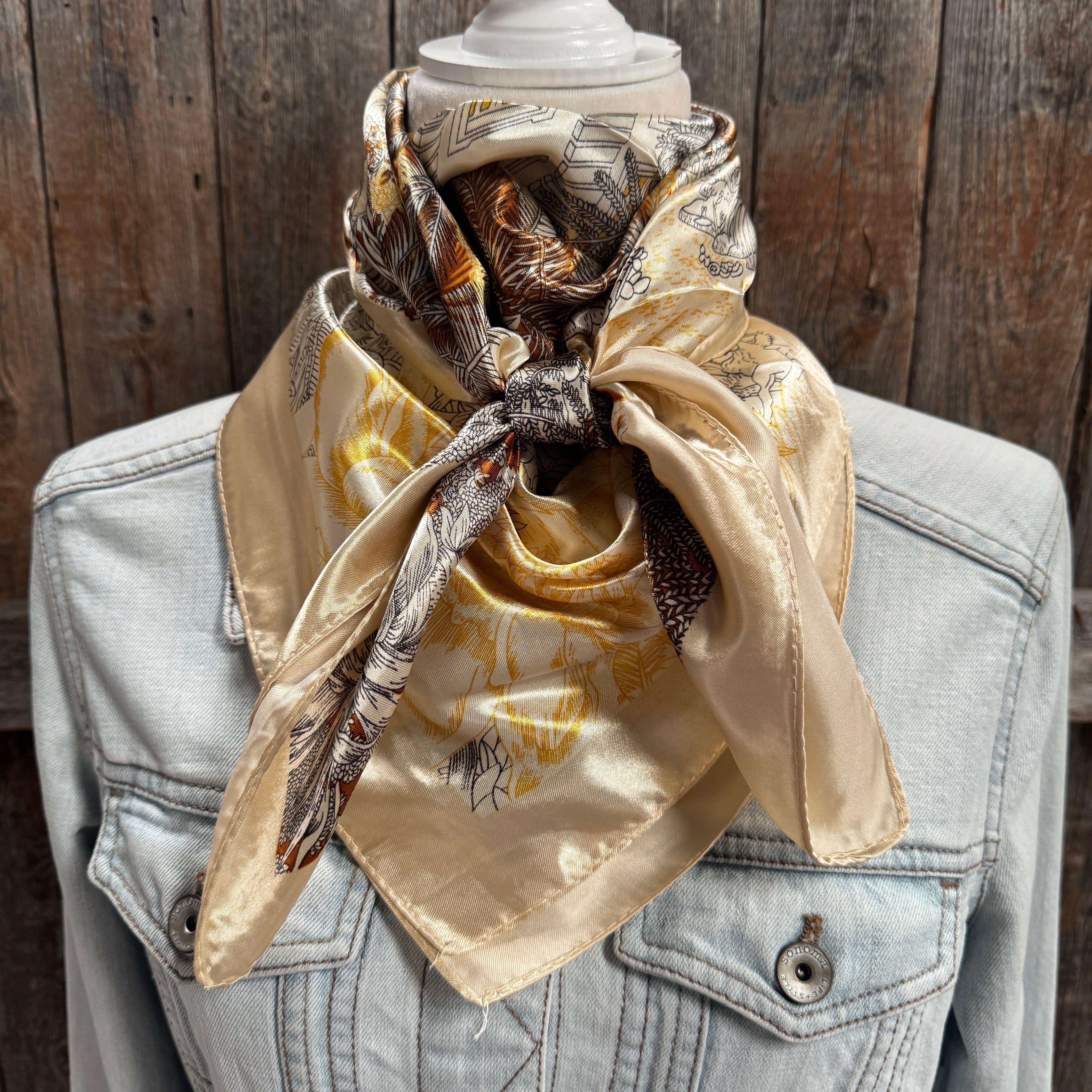Beige scarf with pattern draped over a denim jacket against a wooden background