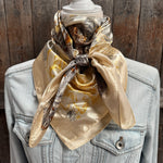 Beige scarf with pattern draped over a denim jacket against a wooden background