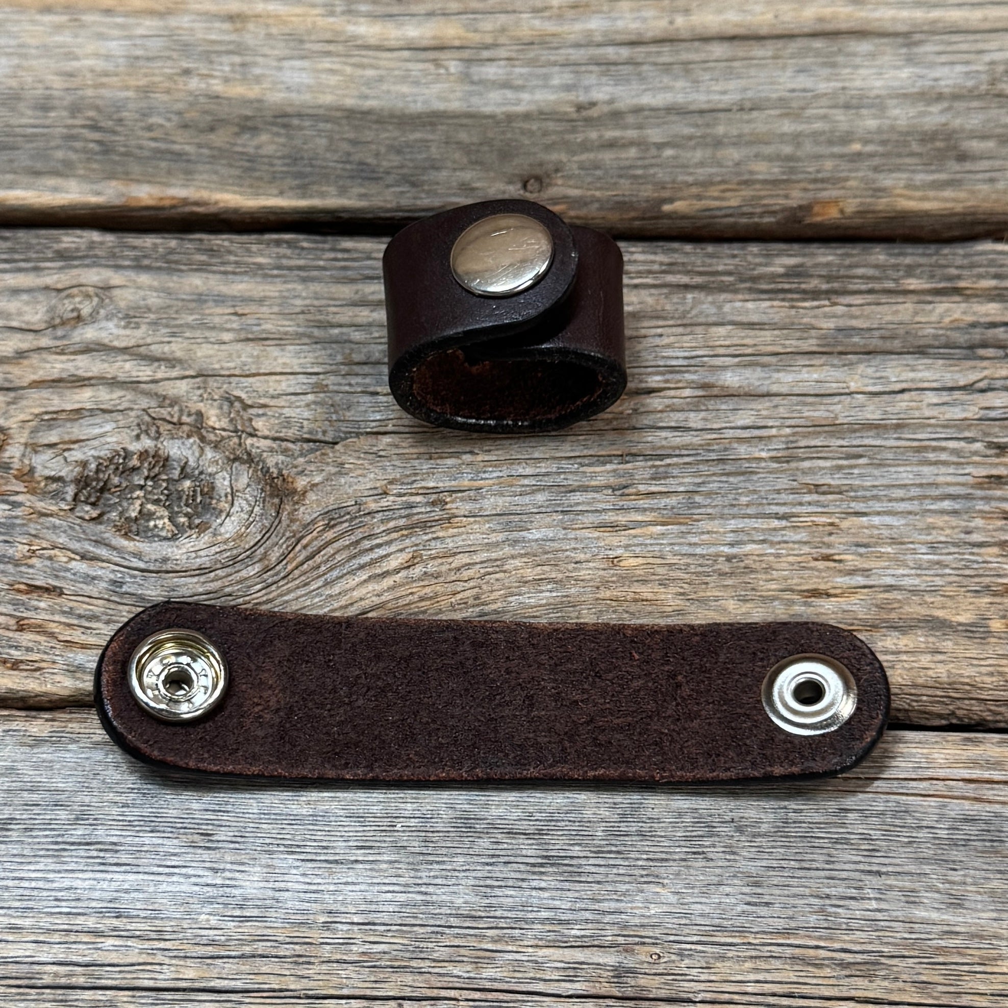 a brown leather band with two silver buttons on a wooden surface.