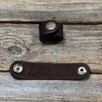 a brown leather band with two silver buttons on a wooden surface.