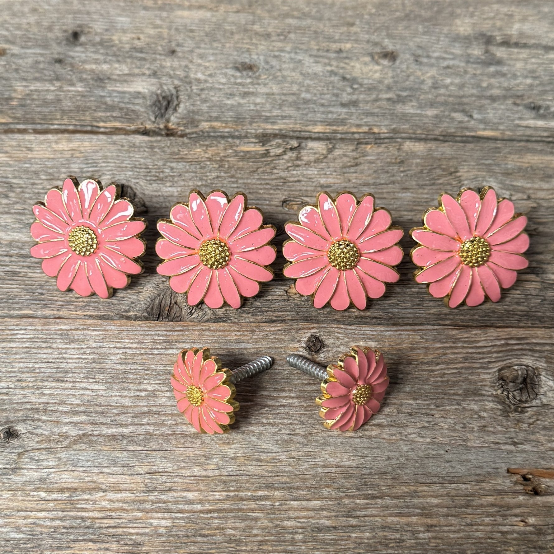 a collection of pink enamel flower-shaped objects arranged on a wooden surface.