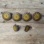 a collection of decorative metal buttons with yellow and black floral designs, arranged on a wooden surface.