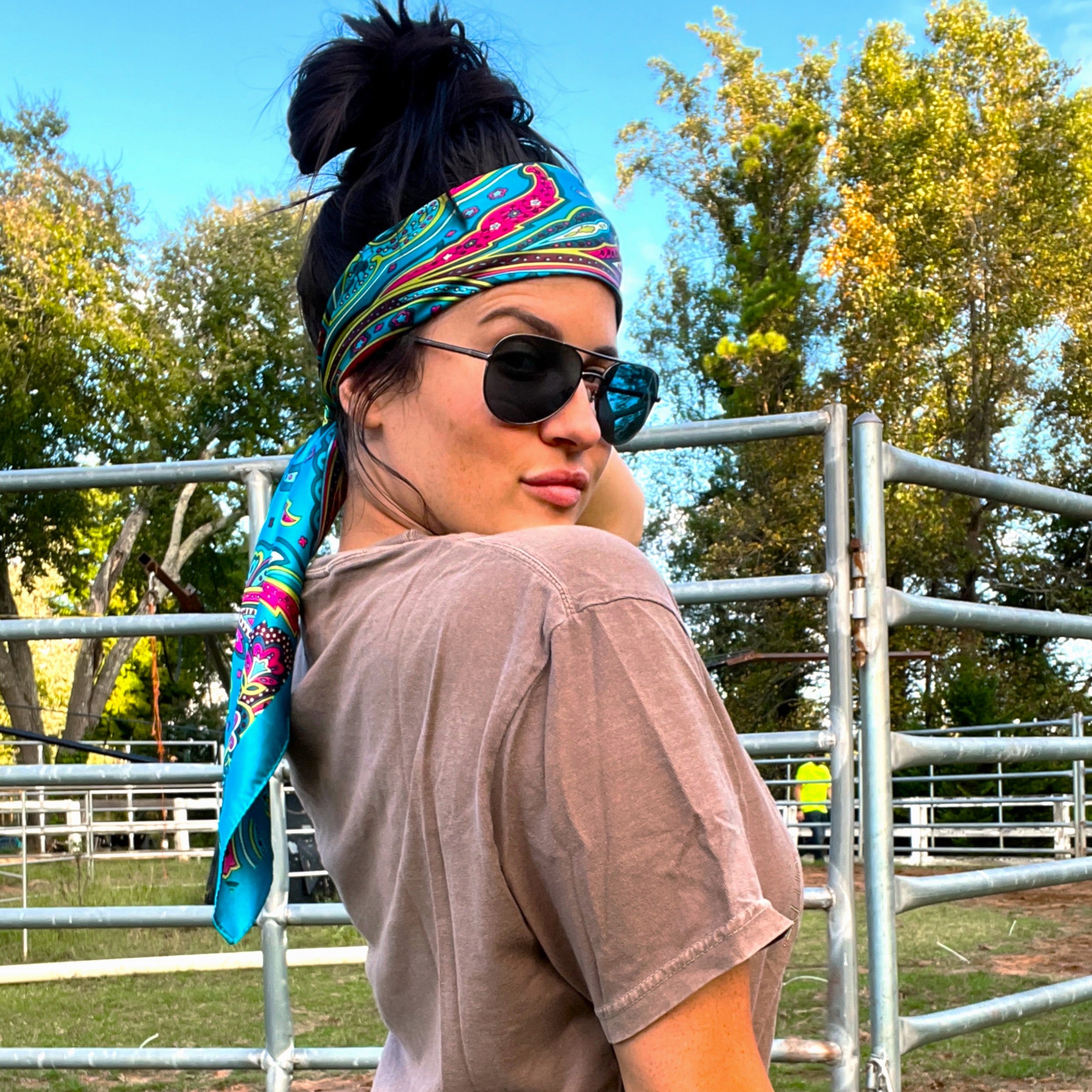 Person wearing sunglasses and a colorful headband in an outdoor setting with trees and a fence.